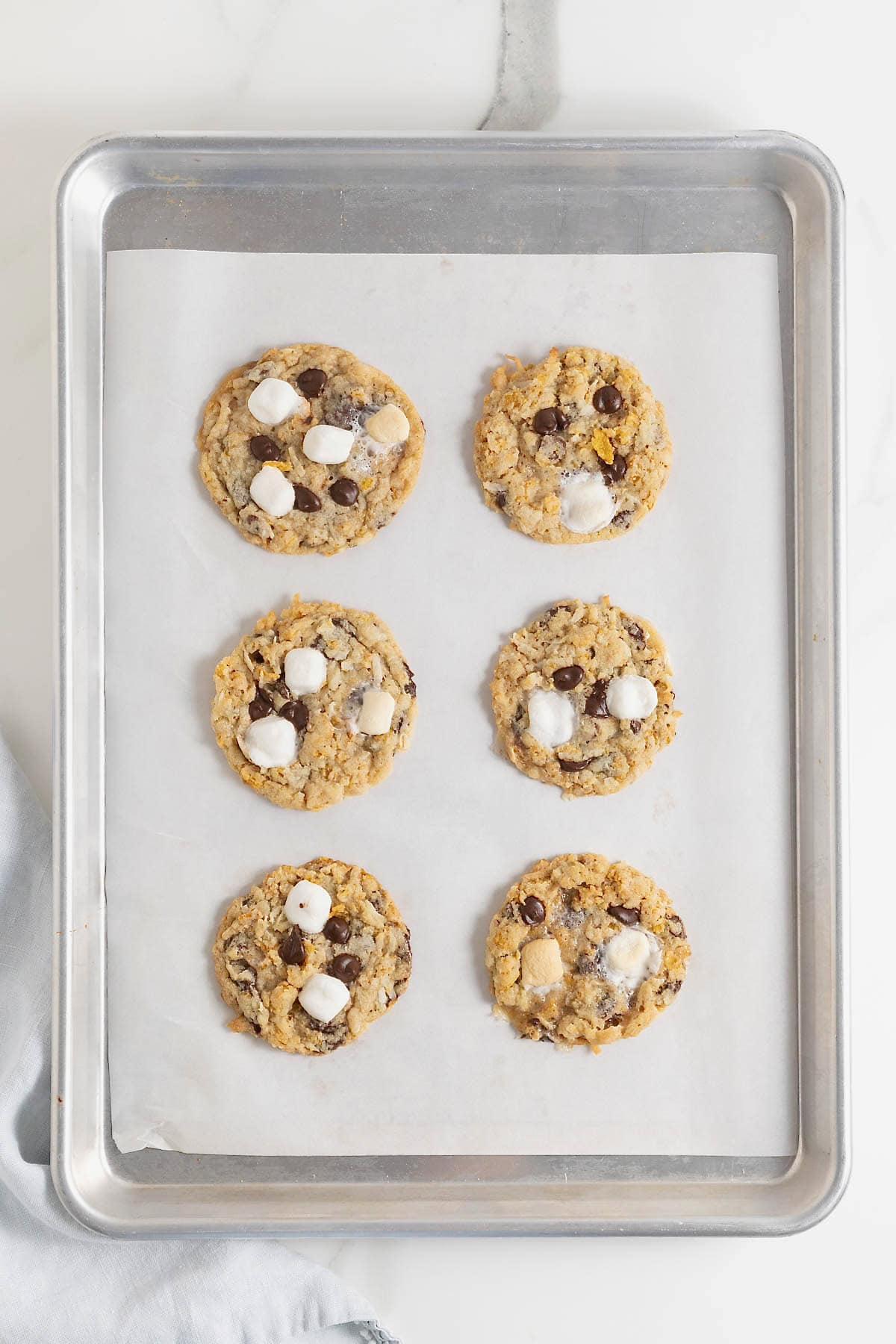 Six chocolate chip corn flake coconut cookies on a parchment lined baking sheet.