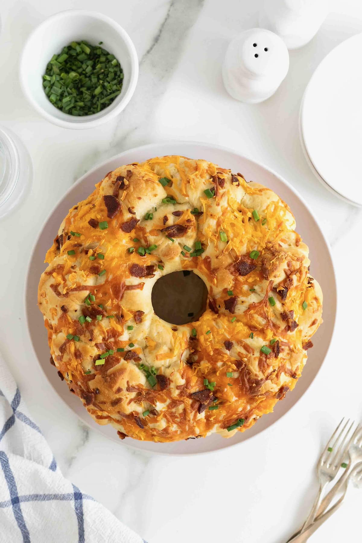 A bacon and cheddar monkey bread garnished with chives on a large white plate.