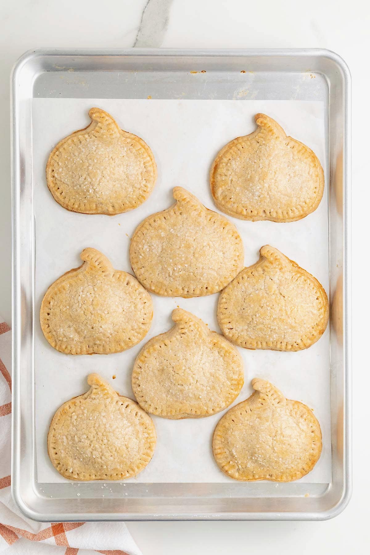 Eight pumpkin hand pies on a parchment lined baking sheet.