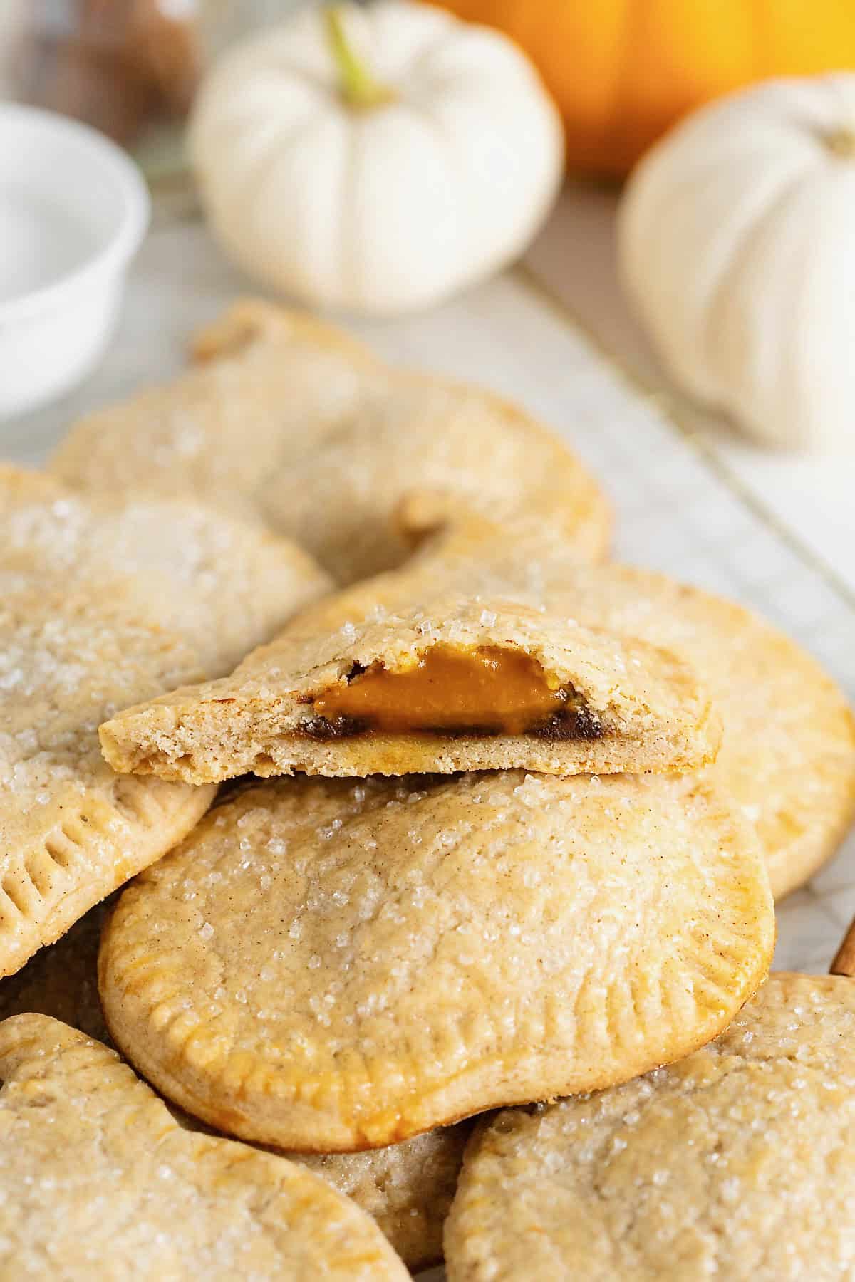 A pile of pumpkin shaped hand pies on a gold toned cooling rack. The top pie has a bite out of it.