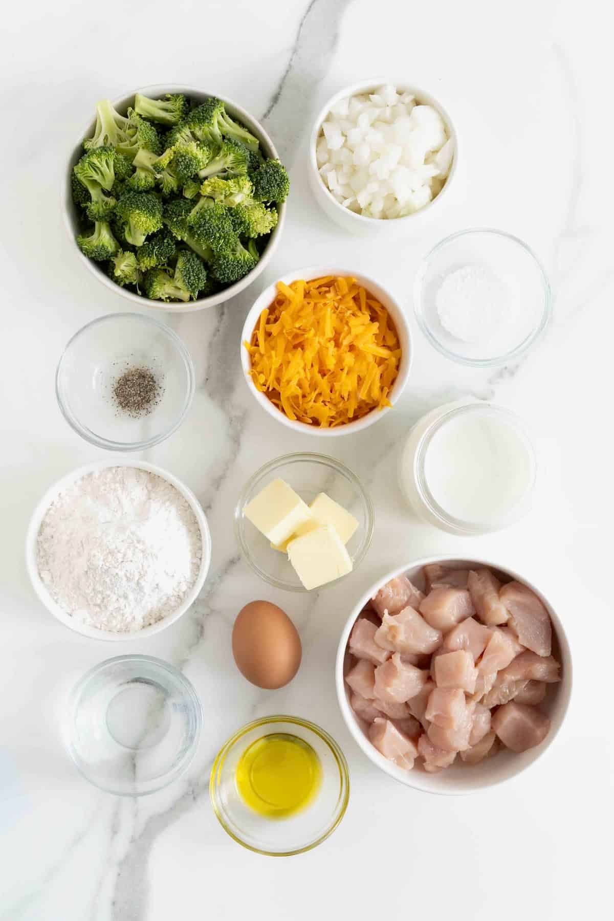 Ingredients to make broccoli cheese pot pie in small glass dishes on a white marble counter.