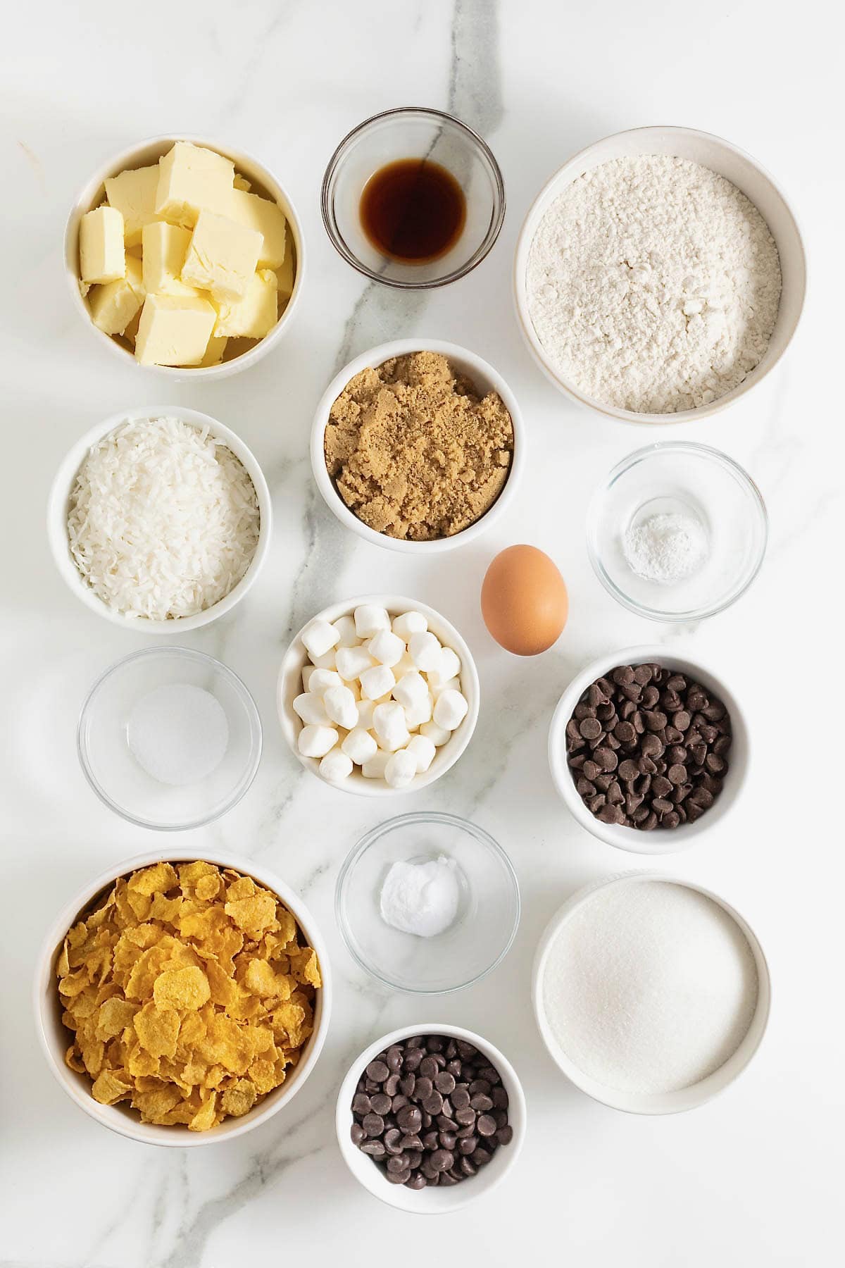 Ingredients for corn flake coconut cookies in small glass dishes on a white marble counter.