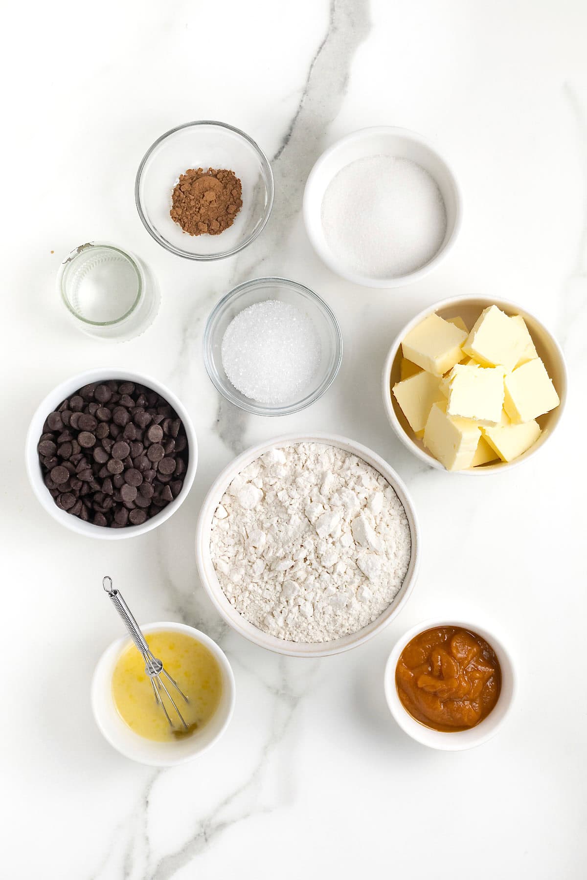 Ingredients to make pumpkin chocolate hand pies in small glass dishes on a white marble counter.