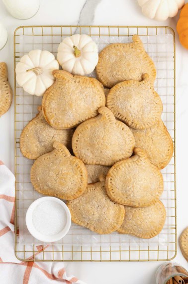 A pile of pumpkin shaped hand pies on a gold toned cooling rack.