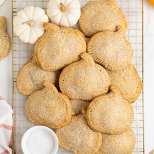 A pile of pumpkin shaped hand pies on a gold toned cooling rack.