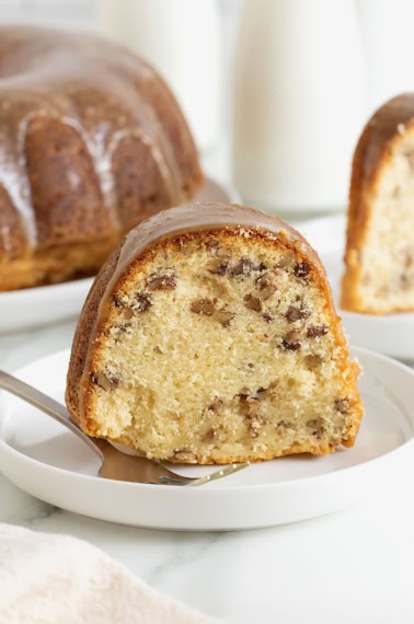 A slice of brown butter pecan pound cake on a white dessert plate. There is a metal fork on the plate.