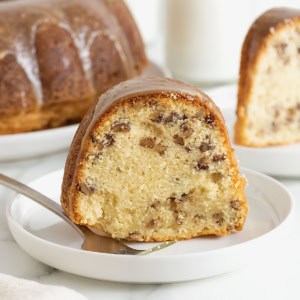 A slice of brown butter pecan pound cake on a white dessert plate. There is a metal fork on the plate.