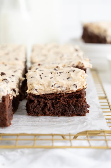 Rich fudge brownies topped with cookie dough frosting on a parchment lined gold-toned cooling rack.