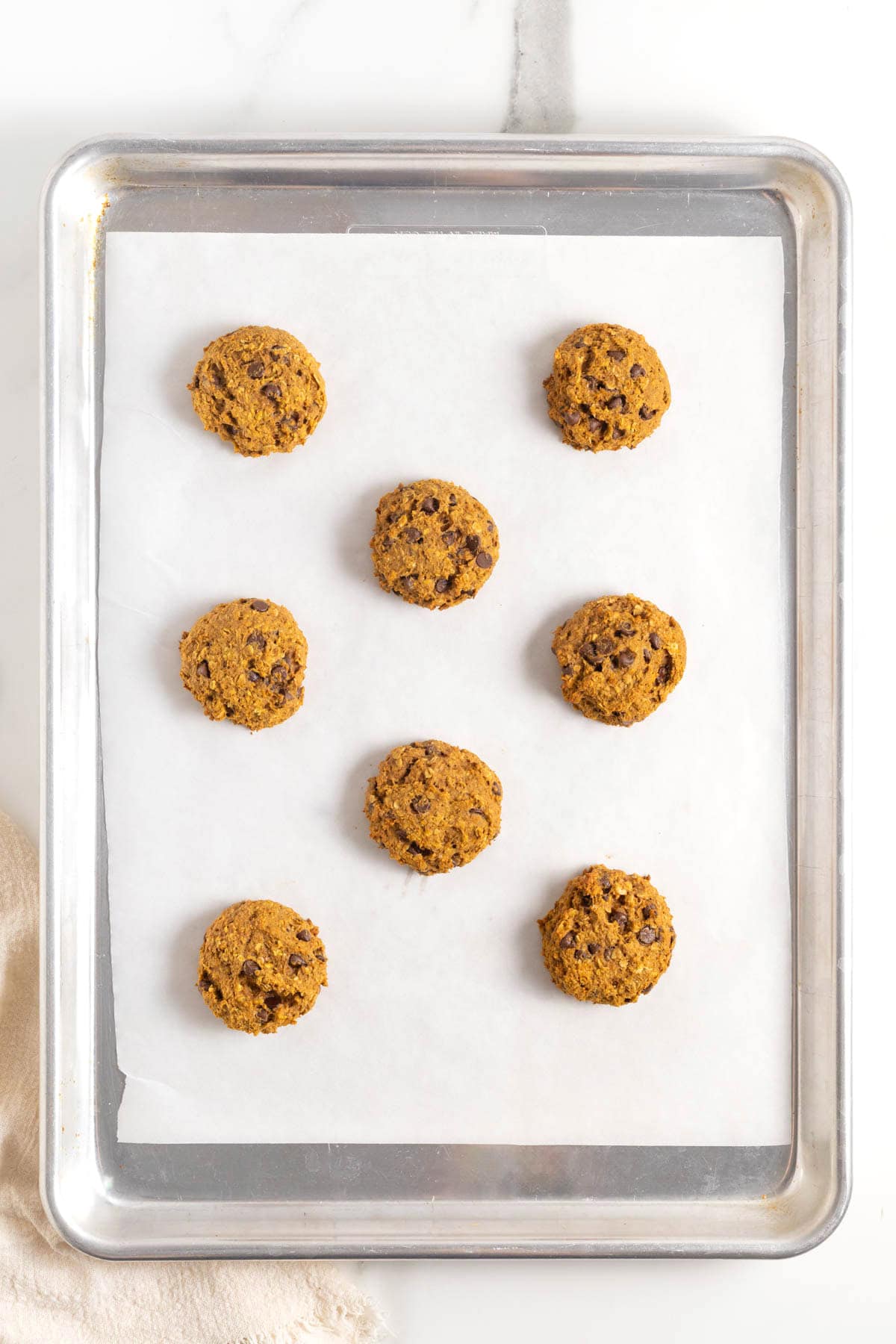 Eight mini pumpkin oatmeal chocolate chip cookies on a parchment lined aluminum baking sheet.