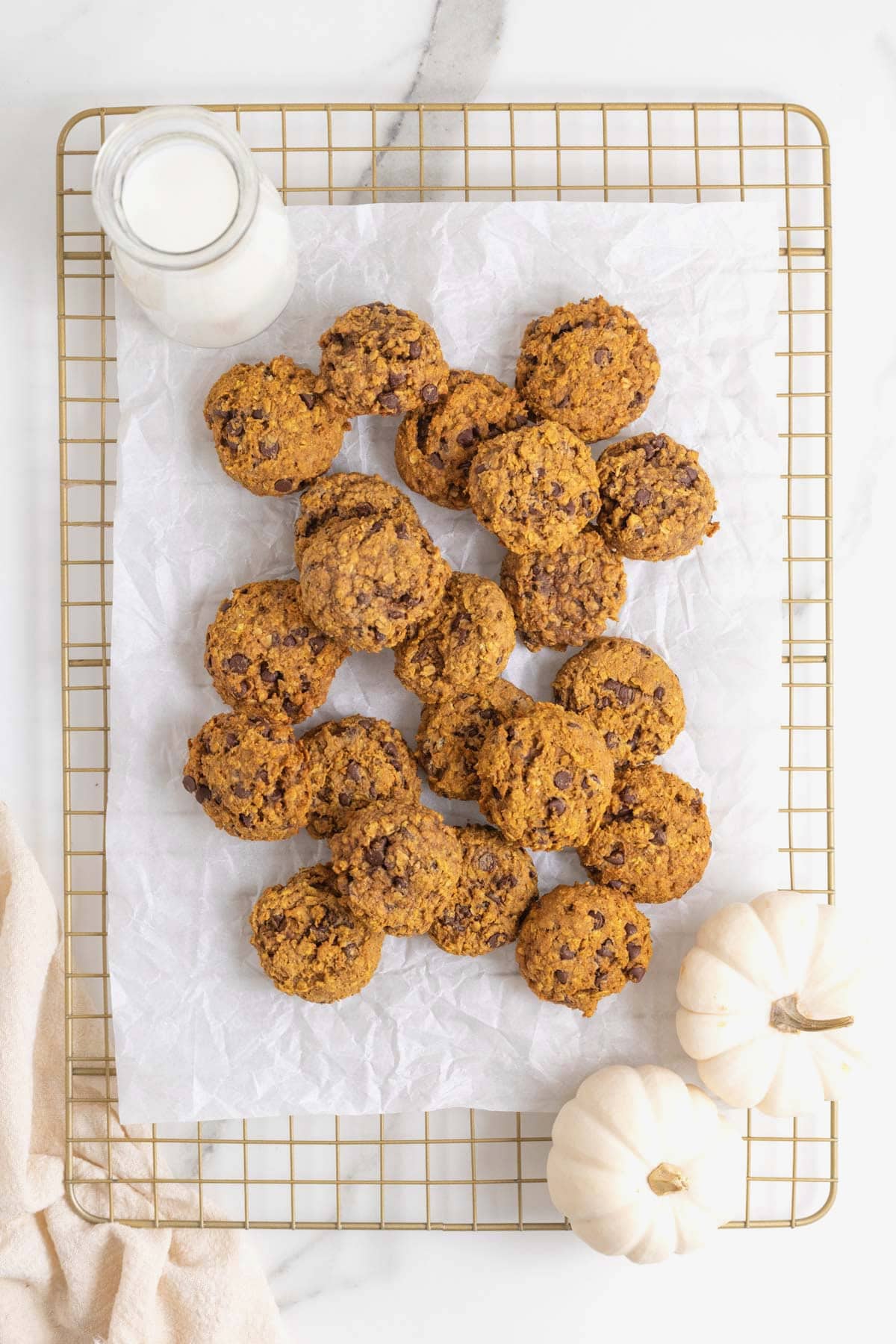 A pile of pumpkin oatmeal cookies on a parchment lined cooling rack.