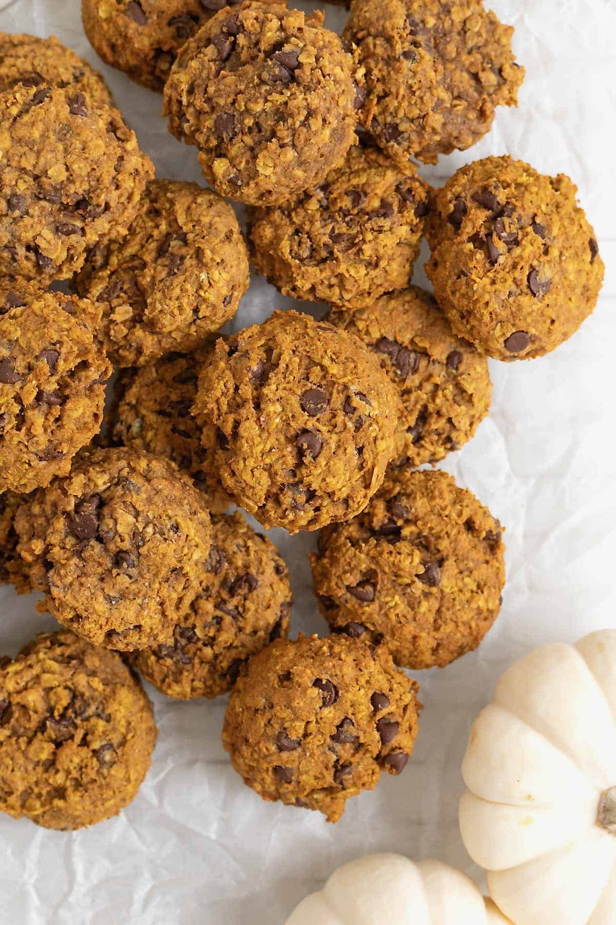 A pile of mini chocolate chip pumpkin oatmeal cookies on a white surface.