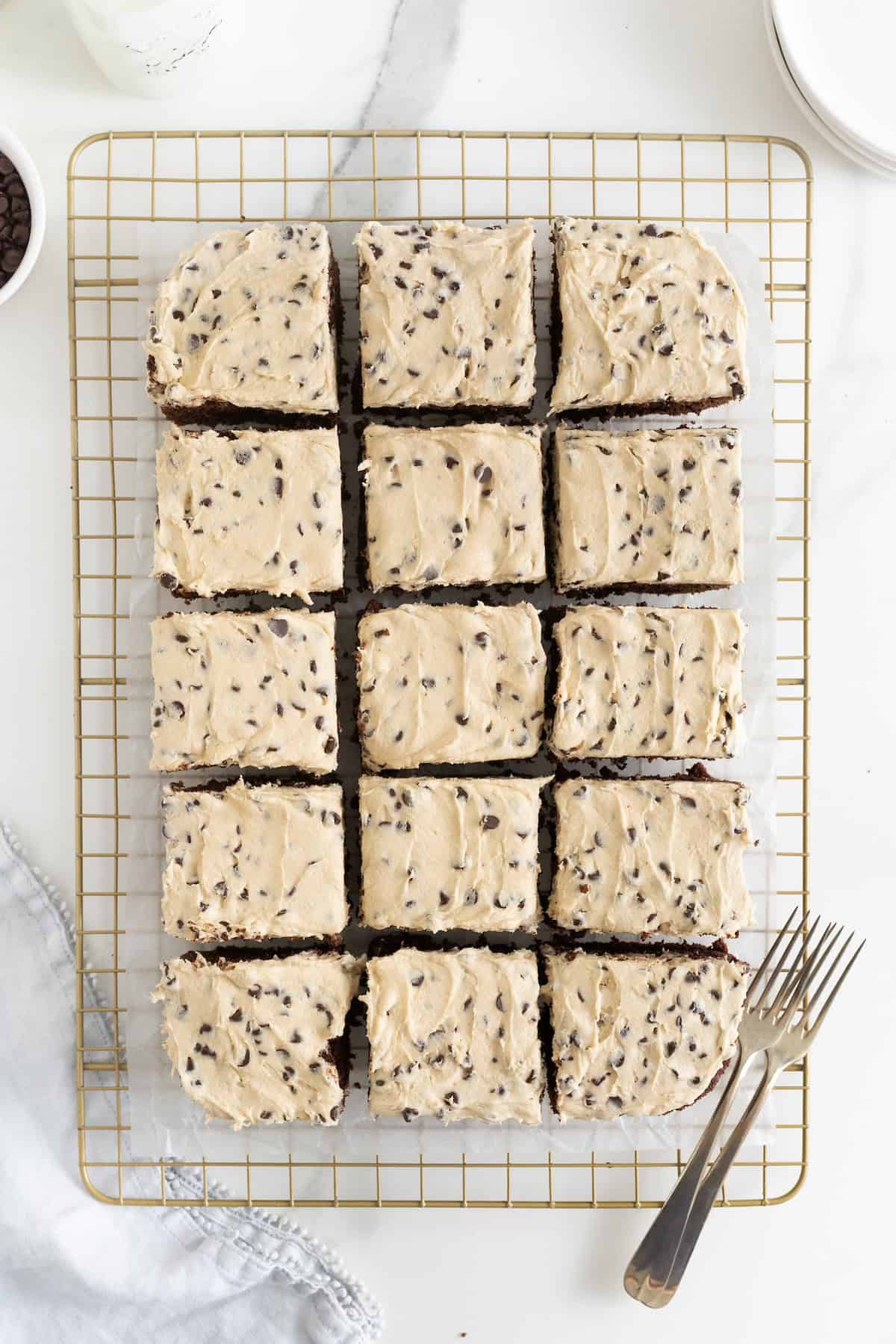 Brownies topped with cookie dough frosting cut into 12 squares on a gold toned cooling rack.