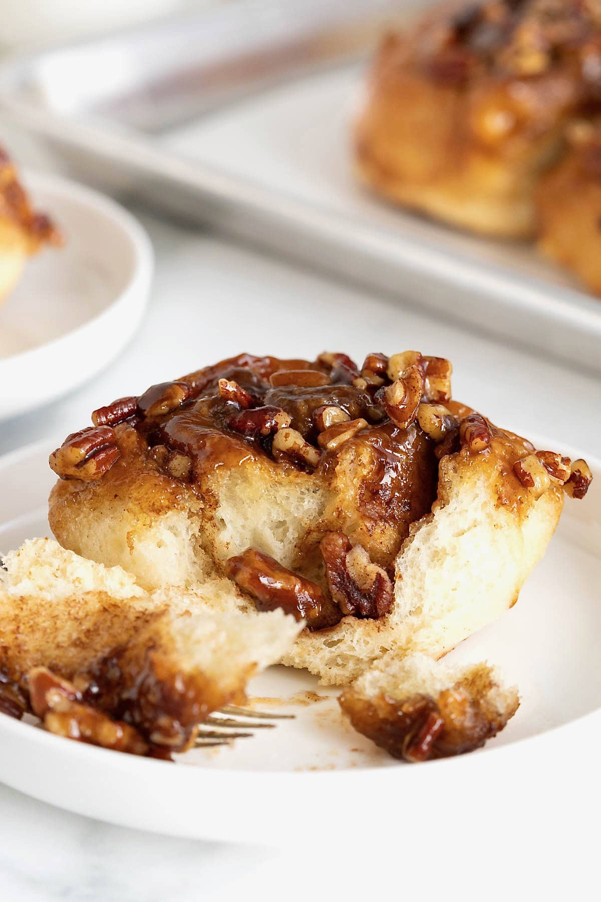 A sticky bun on a white rimmed plate with a fork.