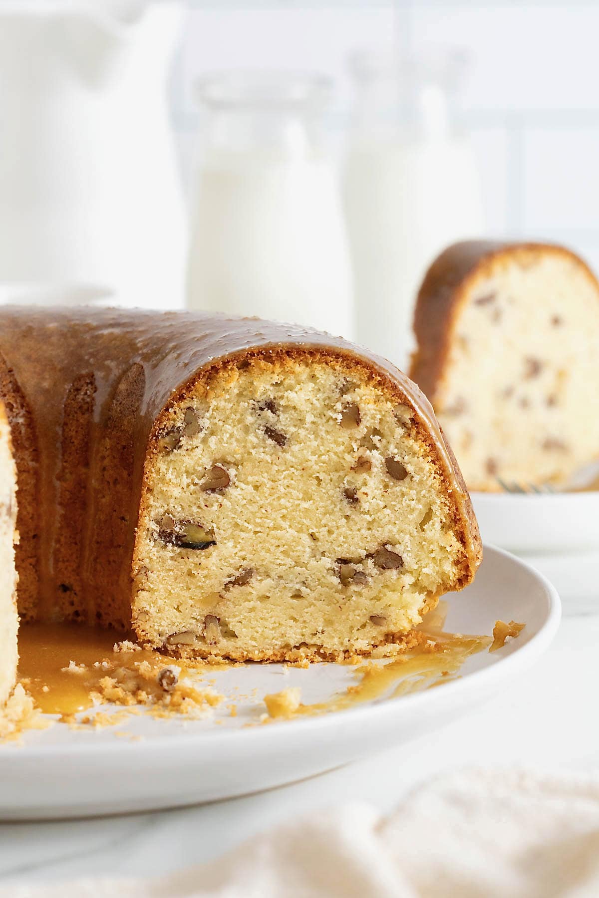 A pecan pound cake with several slices missing on a white cake plate.