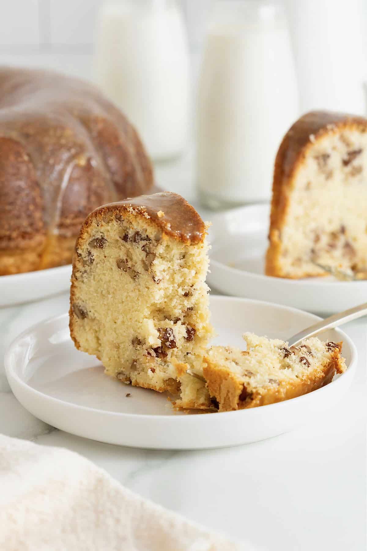 A slice of brown butter pecan pound cake on a white dessert plate with a fork.