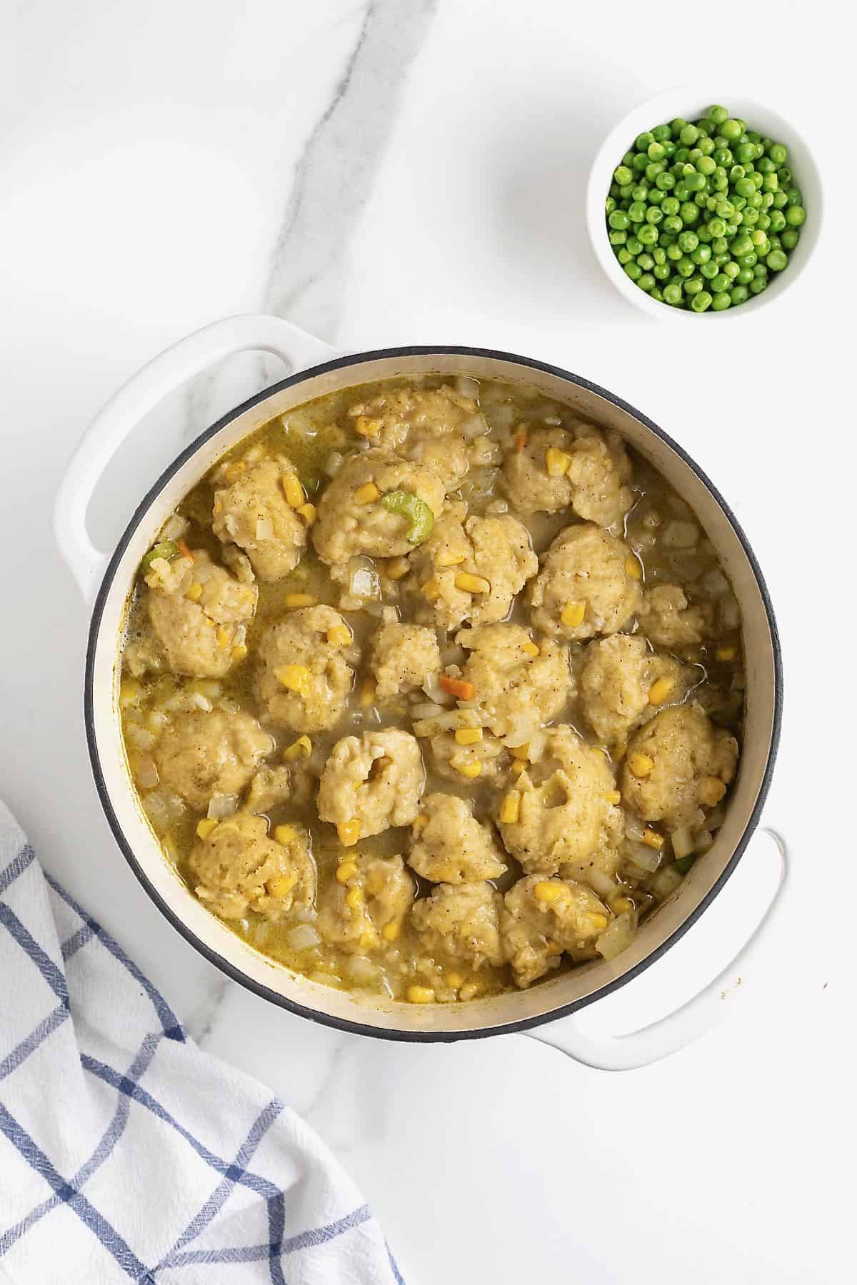 Cornbread dumplings floating in a white dutch oven of turkey and dumplings.