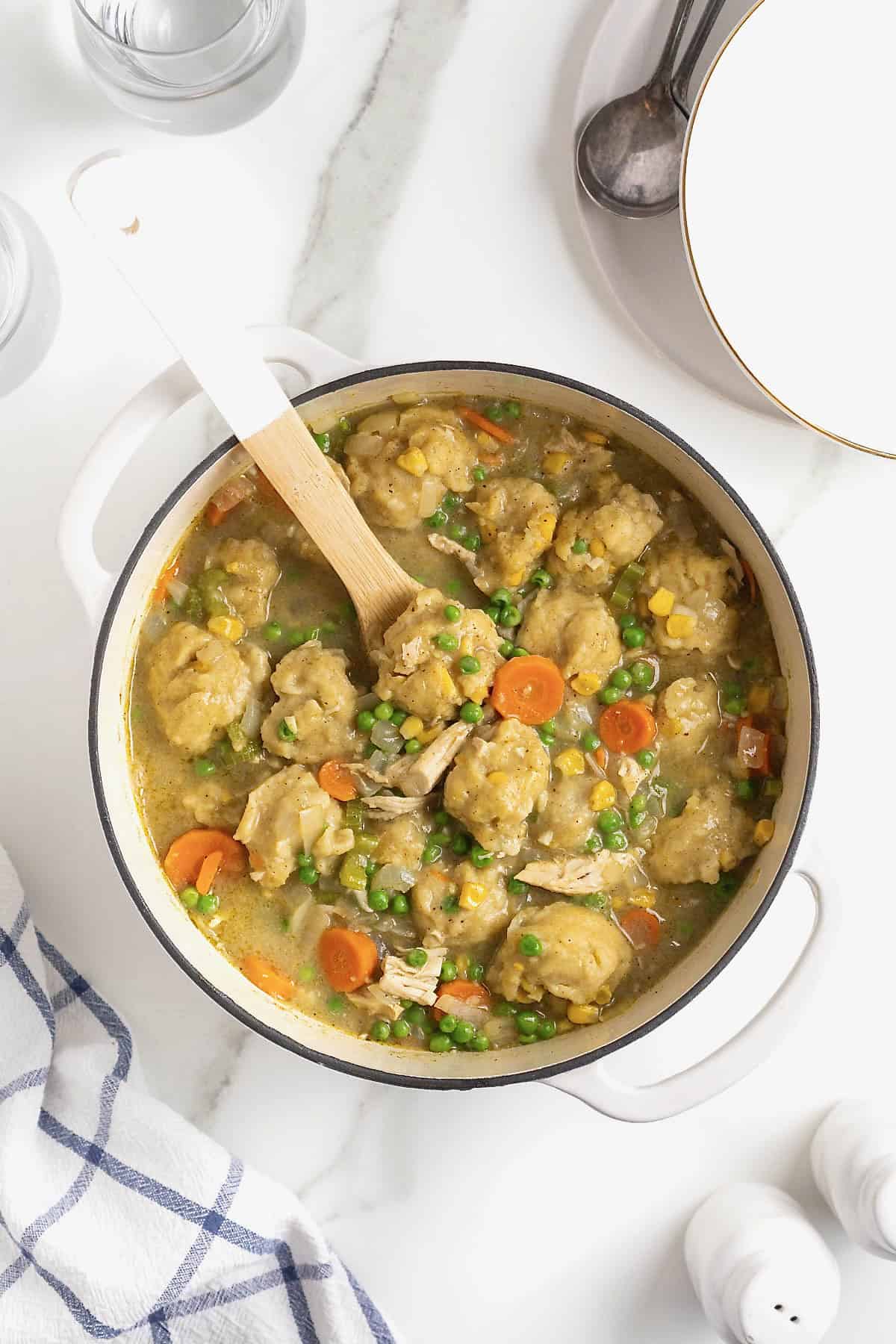 Peas added to a white dutch oven of turkey and dumplings.