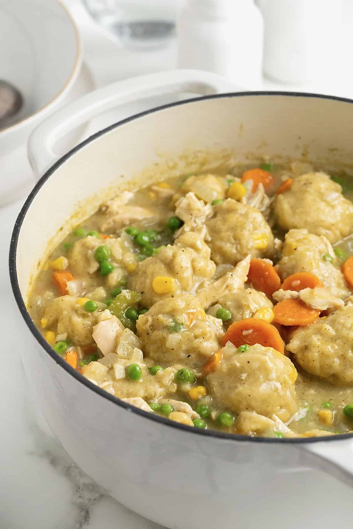 A white Dutch oven of turkey and corn bread dumplings with peas and carrots.
