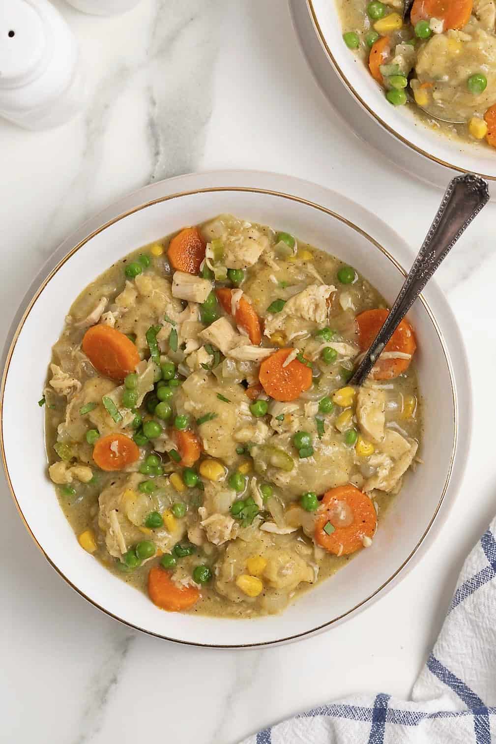 A spoon in a white bowl of turkey and dumplings.