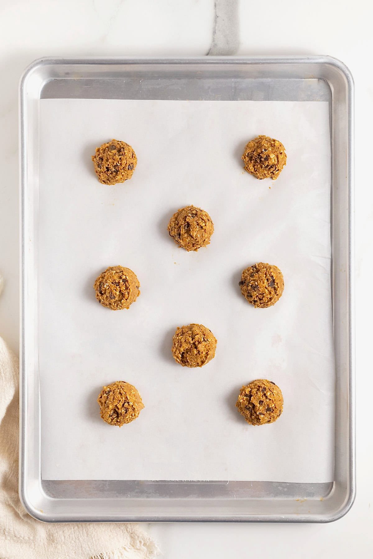 Nine balls of pumpkin oatmeal chocolate chip cookie dough on a parchment lined aluminum cookie sheet.