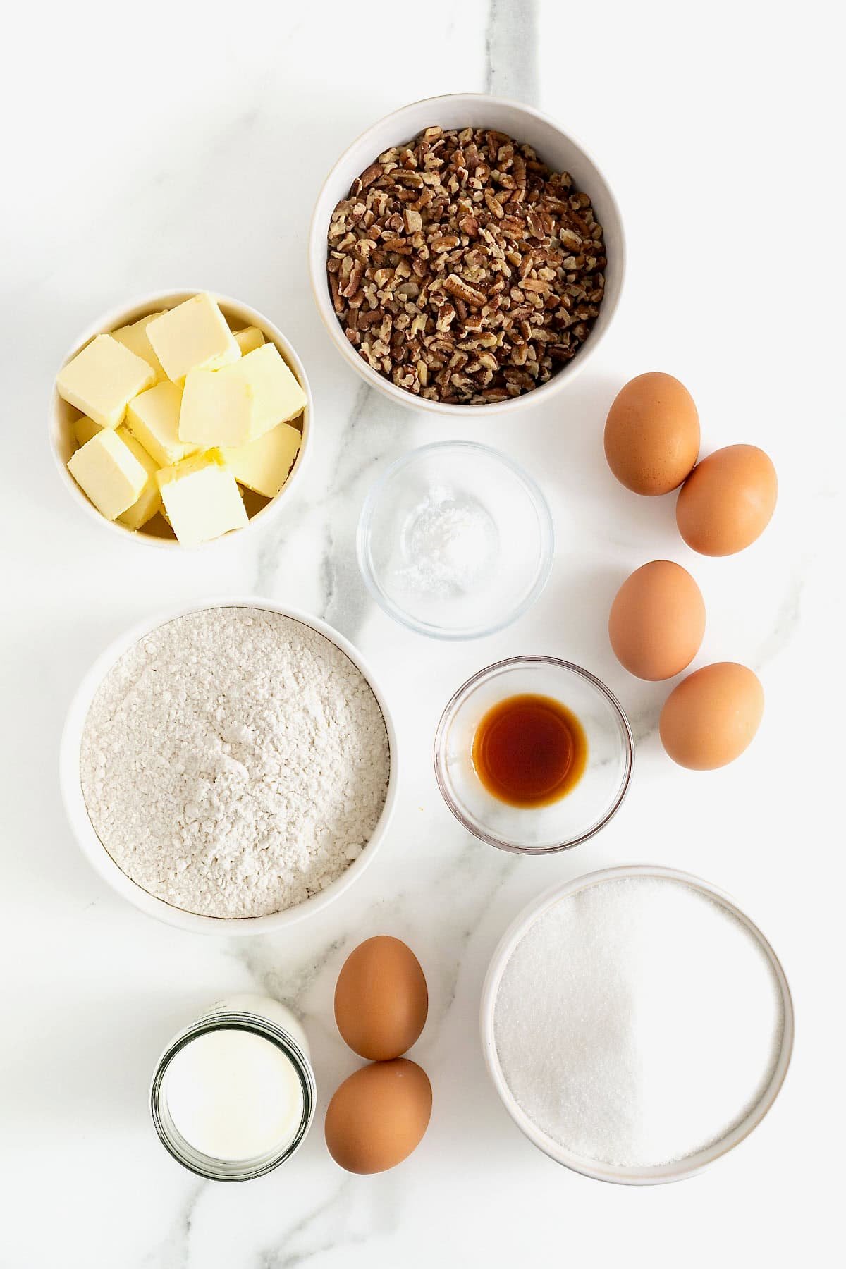 Ingredients to make Brown Butter Pecan Pound Cake in small glass dishes on a white marble counter.
