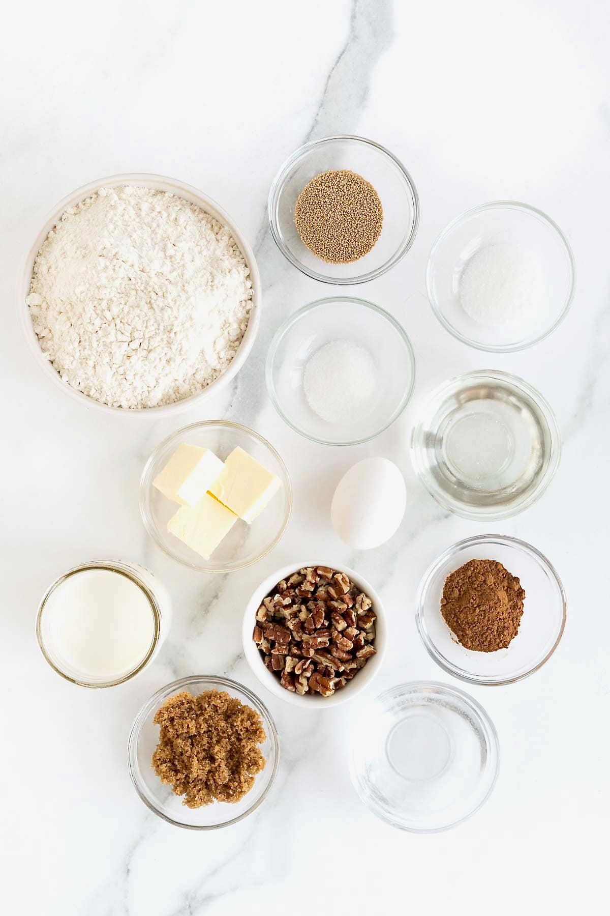 Ingredients to make sticky buns in small glass dishes on a white marble counter.