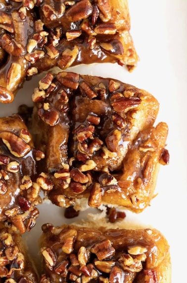 Three sticky buns with chopped pecans on them on a white surface.