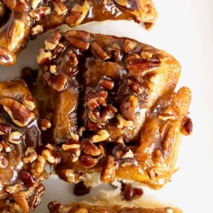 Three sticky buns with chopped pecans on them on a white surface.