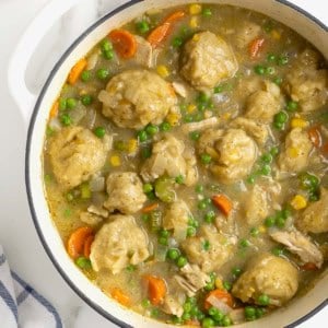 A white Dutch oven of turkey and corn bread dumplings with peas and carrots.
