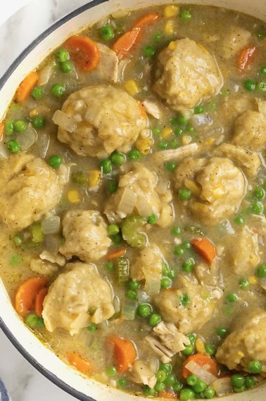 A white Dutch oven of turkey and corn bread dumplings with peas and carrots.