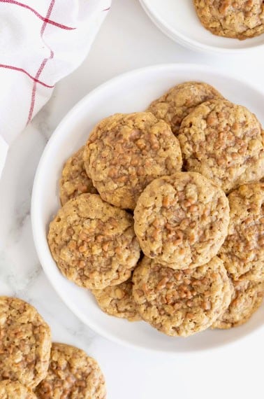 A large white plate of oatmeal toffee cookies on a white marble counter.