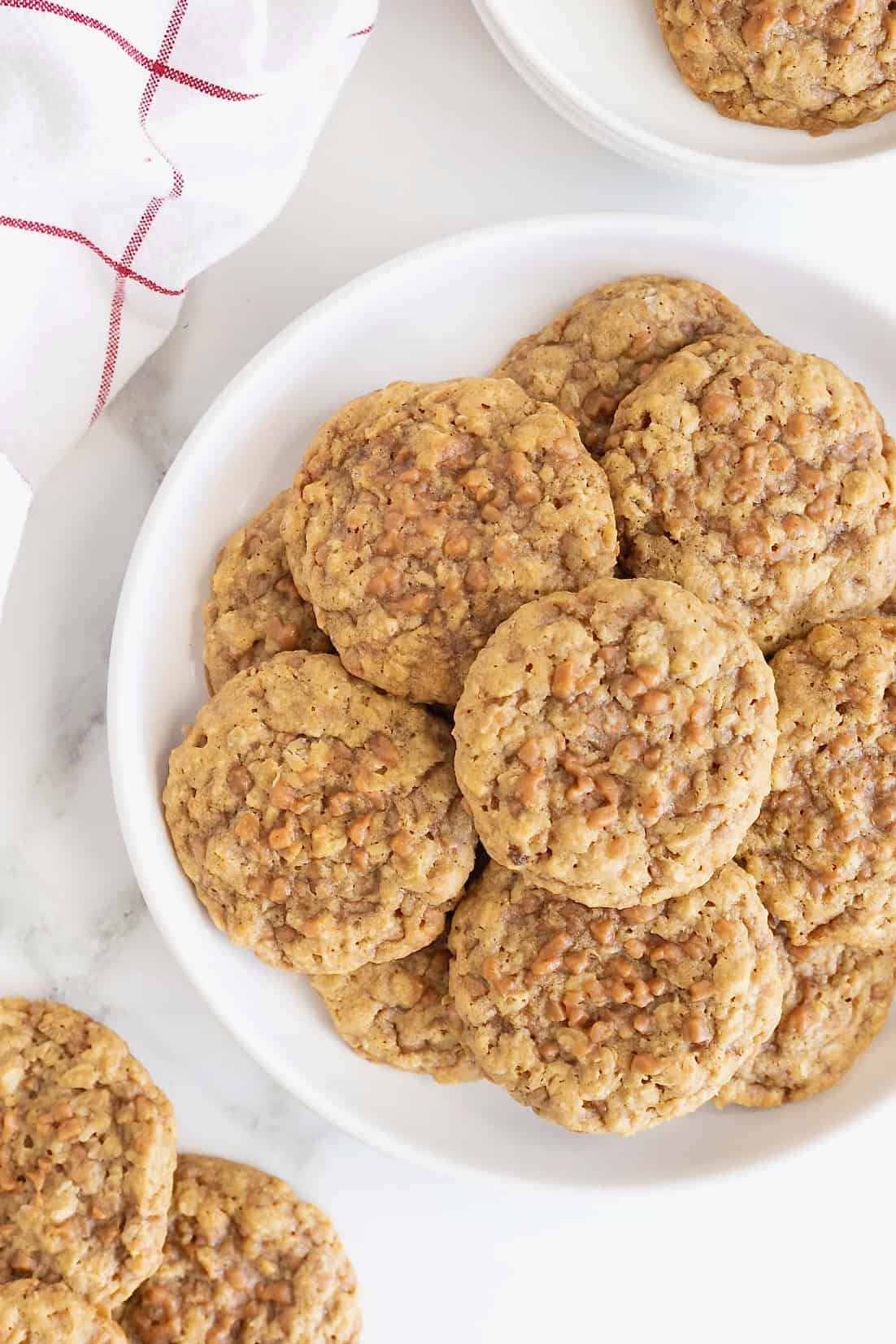 A large white plate of oatmeal toffee cookies on a white marble counter.