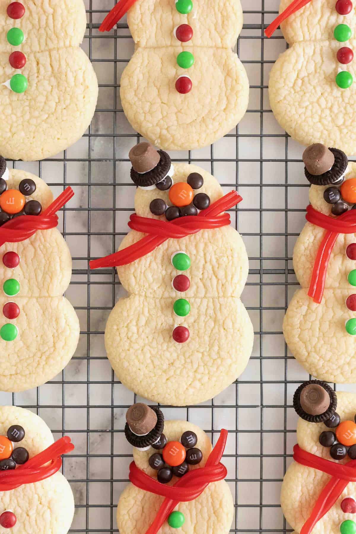 Snowmen shaped sugar cookies decorated with candies on a wire cooling rack.