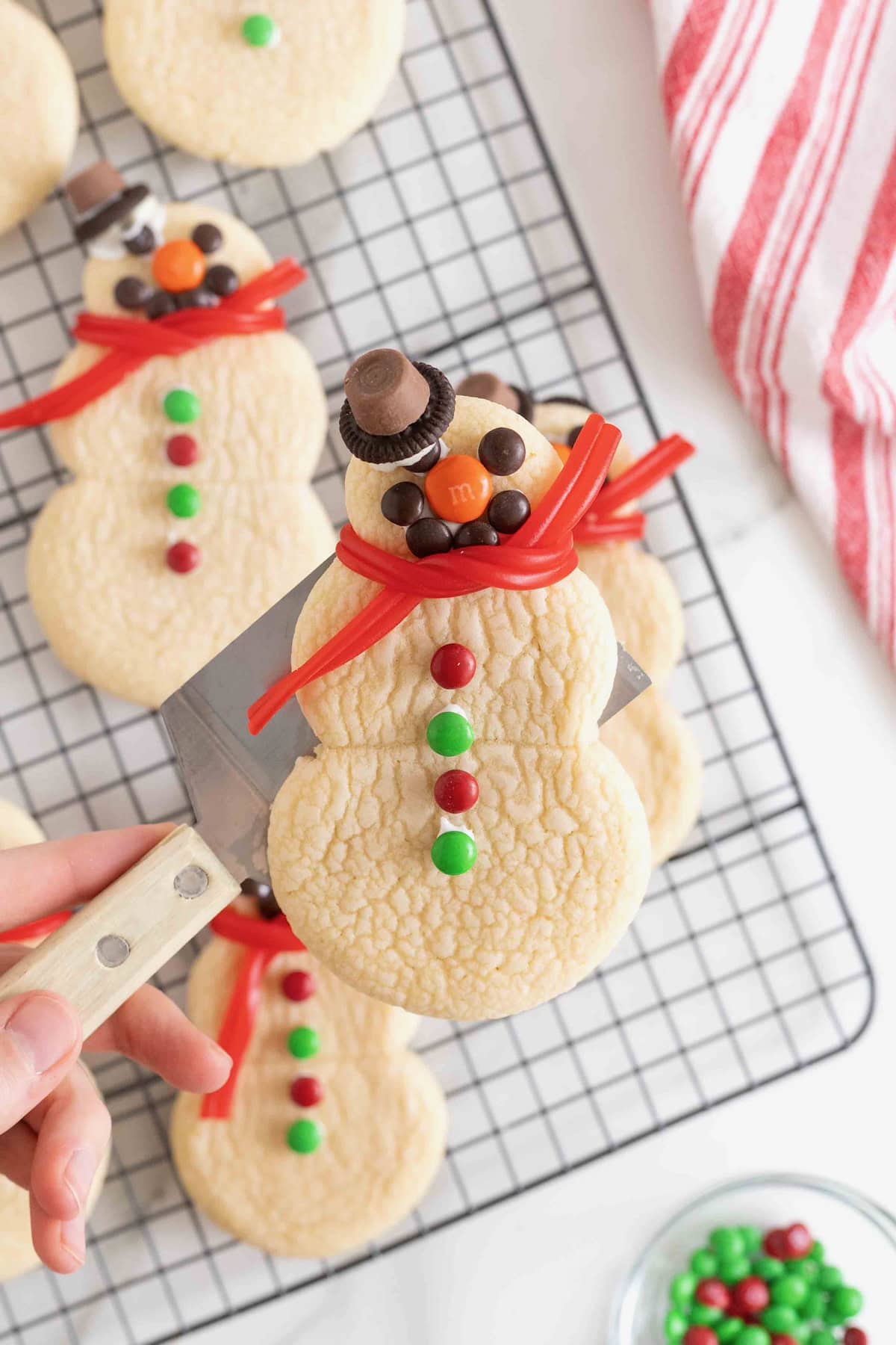 Snowmen shaped sugar cookies decorated with candies on a wire cooling rack.