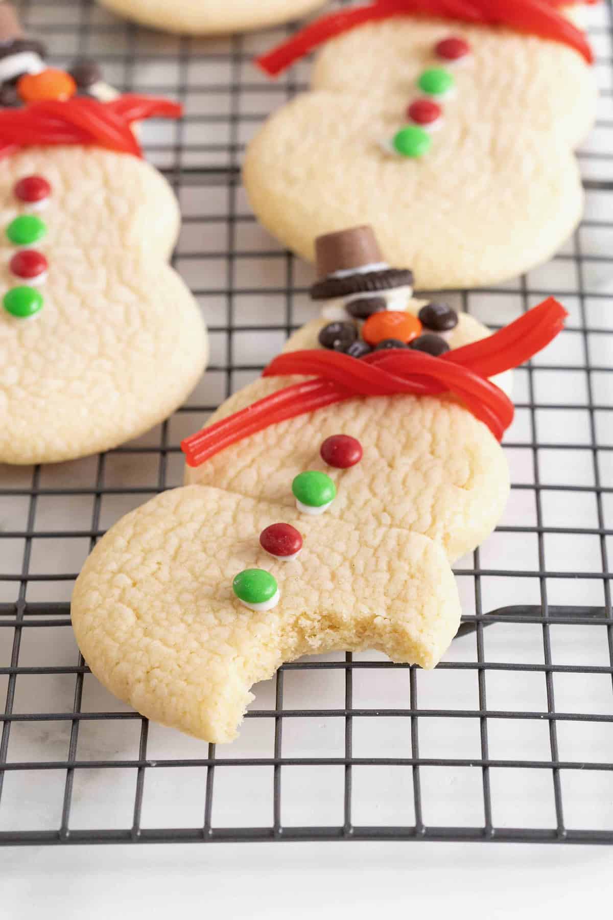 A bite taken out of a snowman shaped sugar cookie on a wire cooling rack.