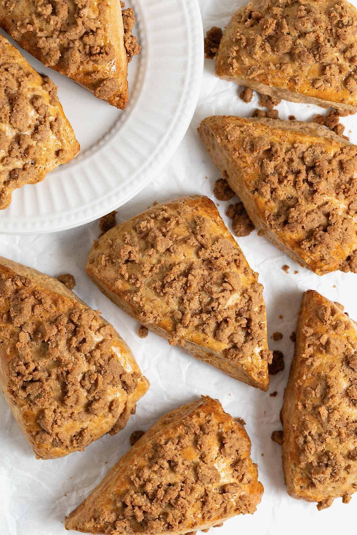 Five snickerdoodle streusel scones on a white surface. There are two more scones on a white plate in the upper left of the photograph.