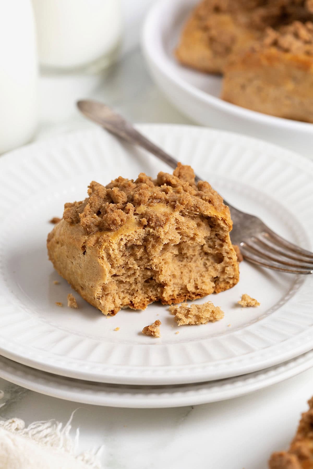 A snickerdoodle scone on a white plate with fluted detailing. There is a fork next to the scone and a bite out of the scone.