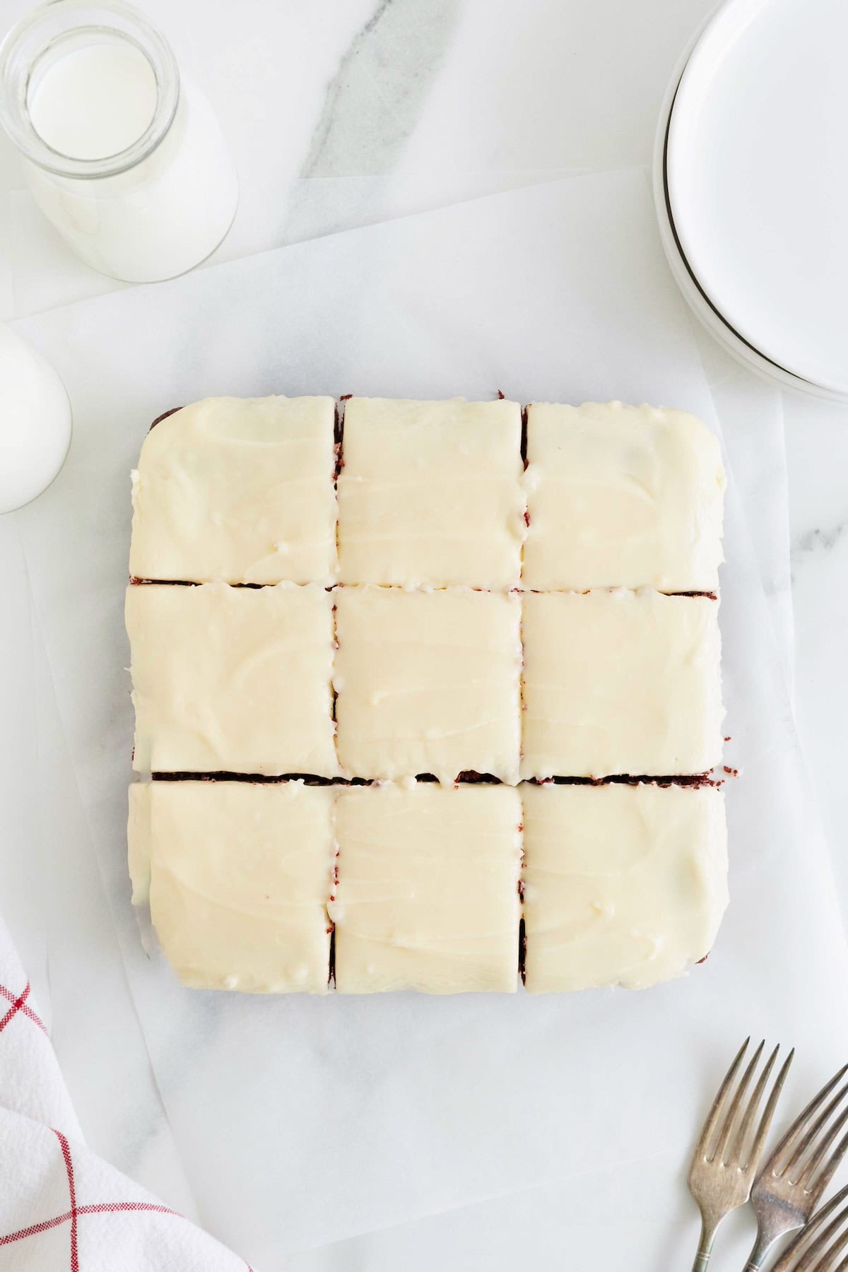 Nine frosted red velvet brownies on a white surface.