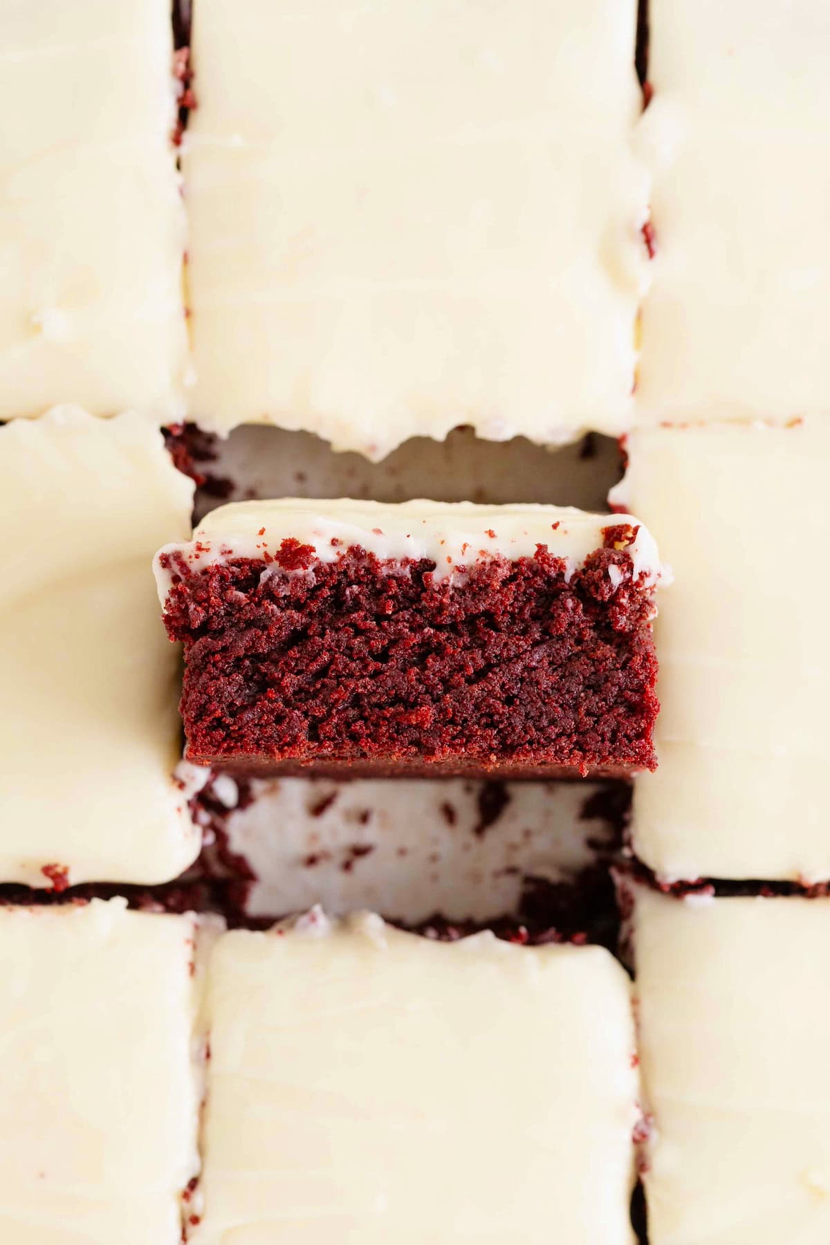 Nine red velvet brownies with white frosting. The center brownie is turned on its side.