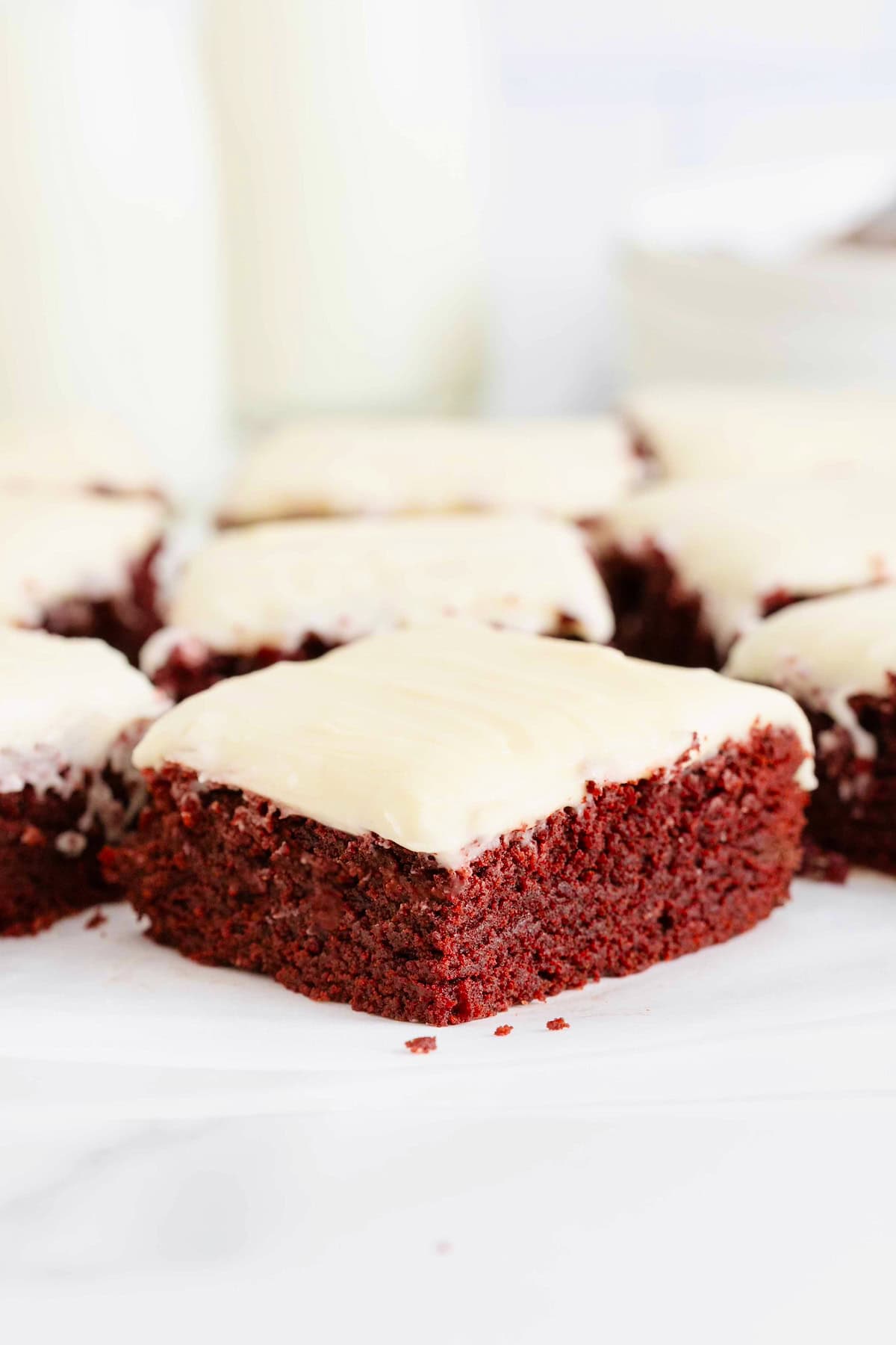 Nine frosted red velvet brownies on a white surface.