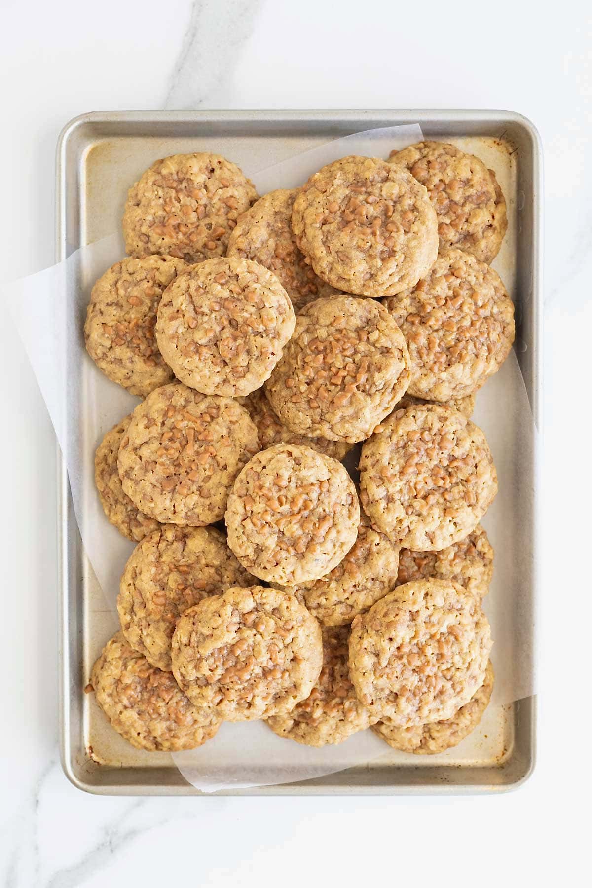 A parchment lined baking sheet piled with oatmeal toffee crunch cookies.