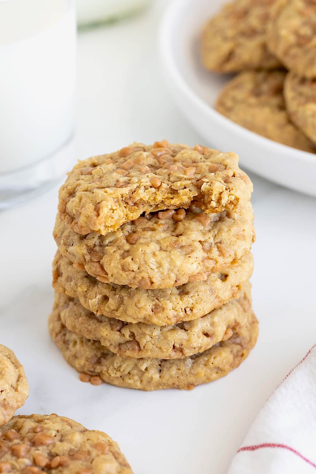 A stack of five oatmeal toffee crunch cookies on a white marble counter. The top cookies has a bite out of it.