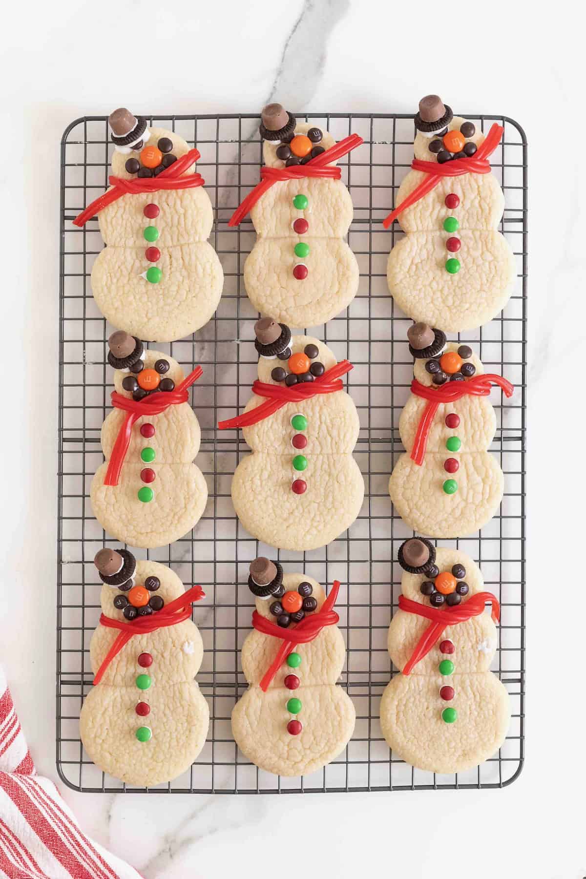 Snowmen shaped sugar cookies decorated with candies on a wire cooling rack.