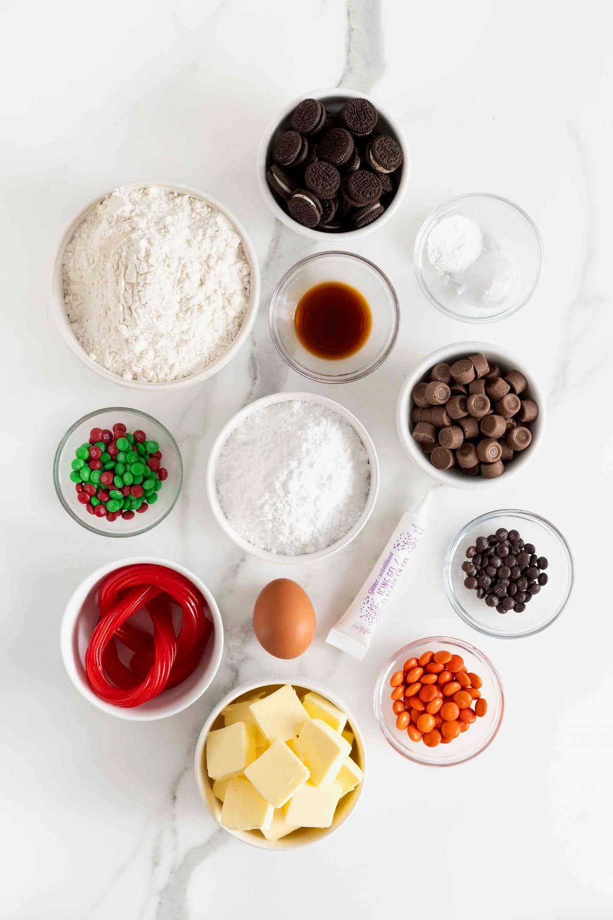 Ingredients to make snowman sugar cookies in small glass dishes on a white marble counter.