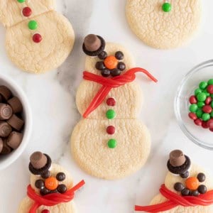 Snowmen shaped sugar cookies decorated with candies on a white marble counter.