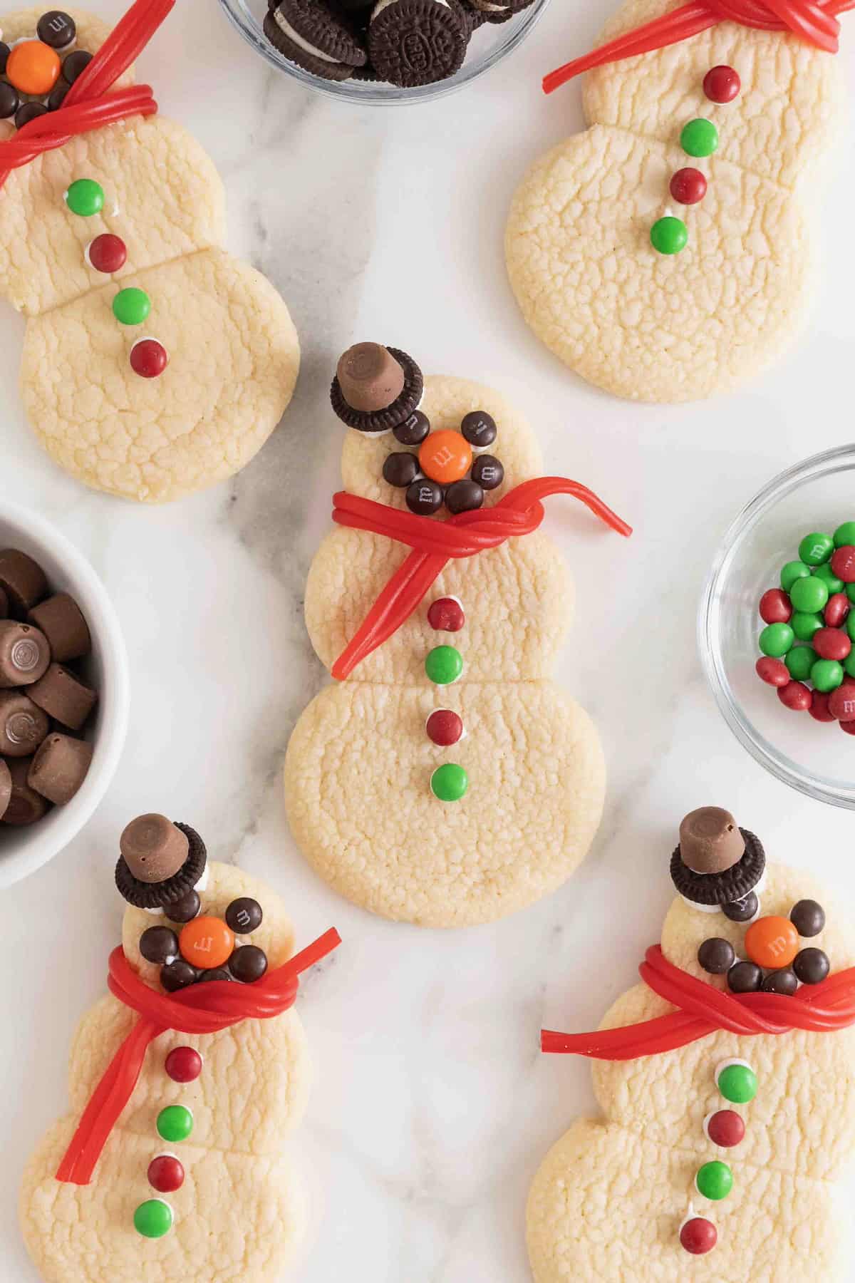 Snowmen shaped sugar cookies decorated with candies on a white marble counter.