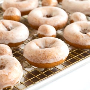 Homemade glazed donuts on a cooling rack over an aluminum sheet pan.