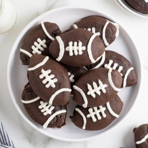 A large white platter of chocolate whoopie pies decorated like footballs.