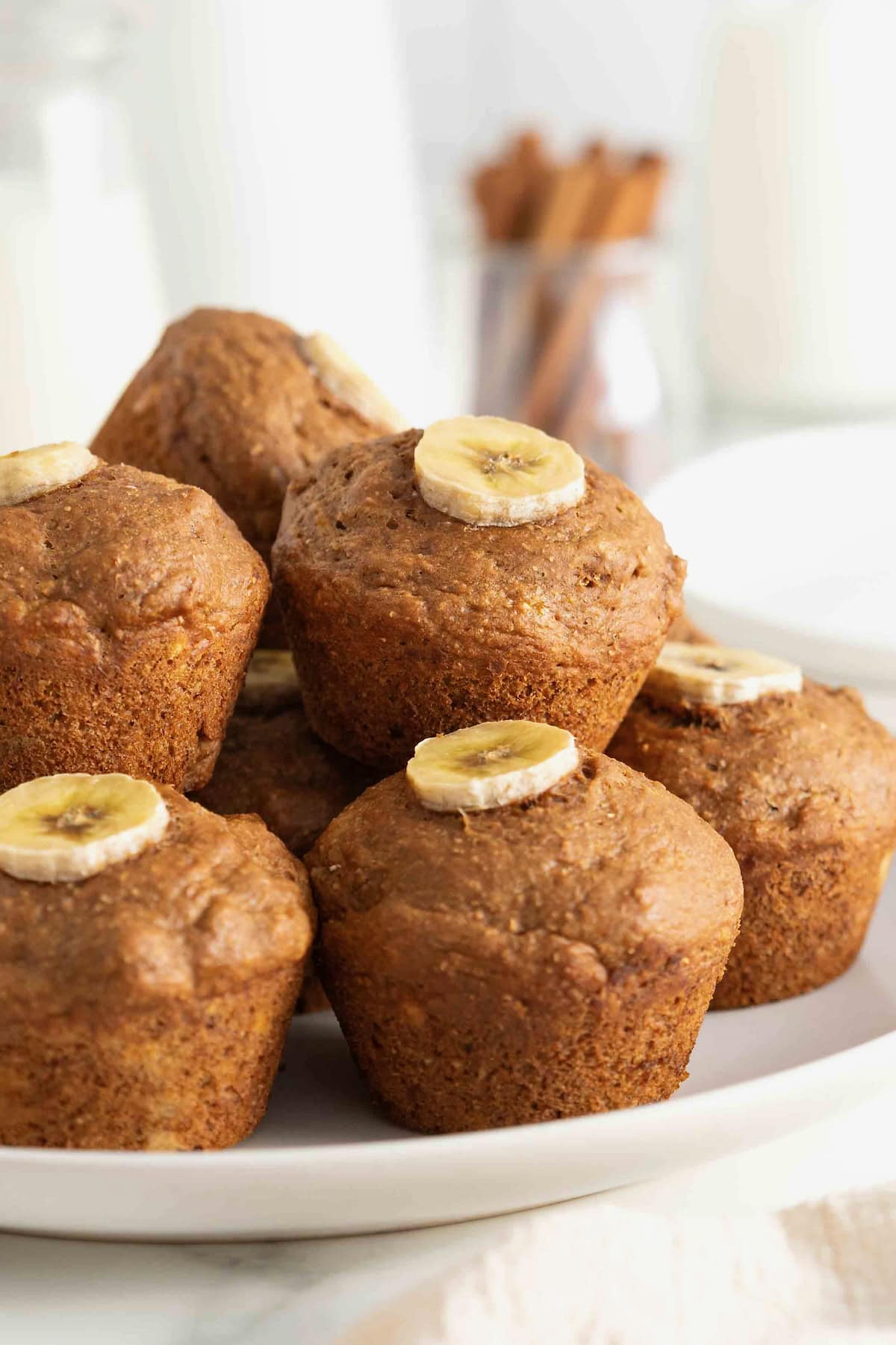 A white serving plate stacked with gingerbread muffins that are garnished with a banana slice.