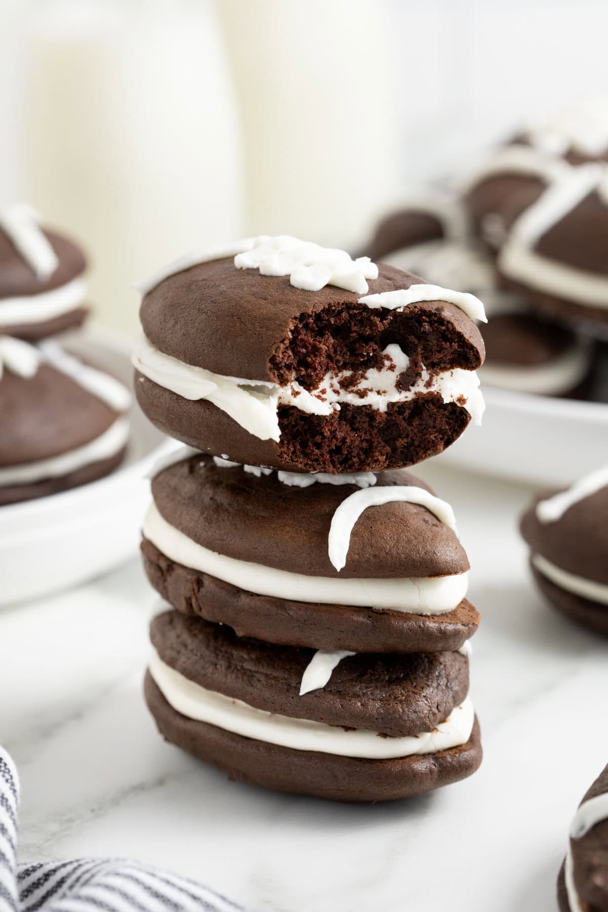 A stack of three football shaped whoopie pies on a white marble counter. The top one has a bite out of it.
